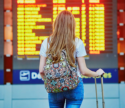 Une jeune femme de dos avec bagages devant un tableau d'affichage de vol