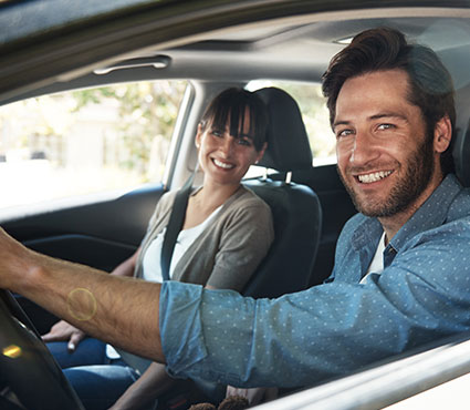 Un homme au volant d'une voiture et une femme côté passagé tout sourire